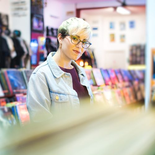 Young Woman Browsing Through Vintage Discs and Choosing Vinyl LP In Records Shop. Portrait of Customer Smiling At Camera And Buying Music Albums.